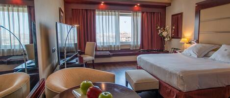 A hotel room with a bed, a desk, a chair, a TV, and a table with apples.
