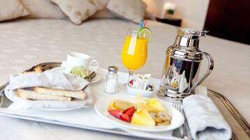 Bandeja de desayuno con tostadas, fruta, un vaso de jugo de naranja y una jarrita plateada sobre la cama.
