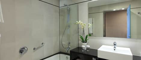 Un baño moderno con ducha envuelta en vidrio, una bañera blanca, un mostrador negro con lavamanos y un espejo sobre el lavamanos.