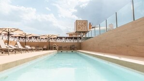 Une piscine avec des chaises longues et des parasols, une terrasse en bois et un panneau sur lequel on peut lire « HC ».