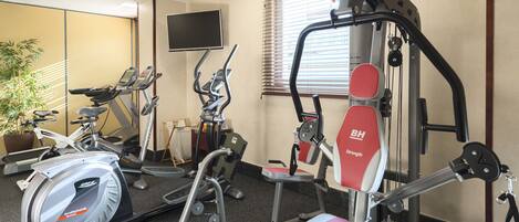 Une salle de sport équipée de machines de cardio, d’appareils de musculation et d’un écran de télévision.