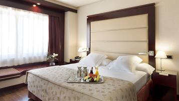 Habitación de hotel con una cama bien hecha, una bandeja con alimentos para el desayuno, una mesita de noche con lámpara y una ventana con cortinas.