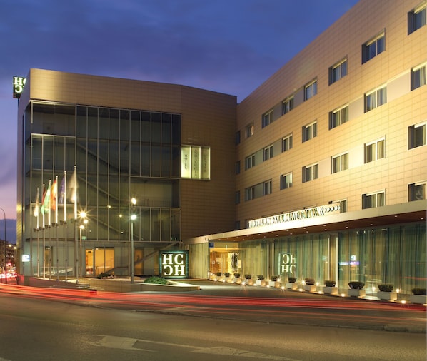 A modern hotel with a curved facade, large glass windows, and a prominent entrance with illuminated signage. - Hotel Andalucia Center (Granada)