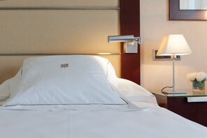 A neatly made bed with white linens, a bedside lamp, and a small vase with white flowers on the nightstand. - Hotel Andalucia Center (Granada)