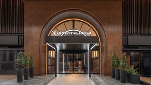 Entrada del Hotel Oriental con un diseño moderno, que presenta fachada de ladrillo, puerta de cristal y plantas en macetas.