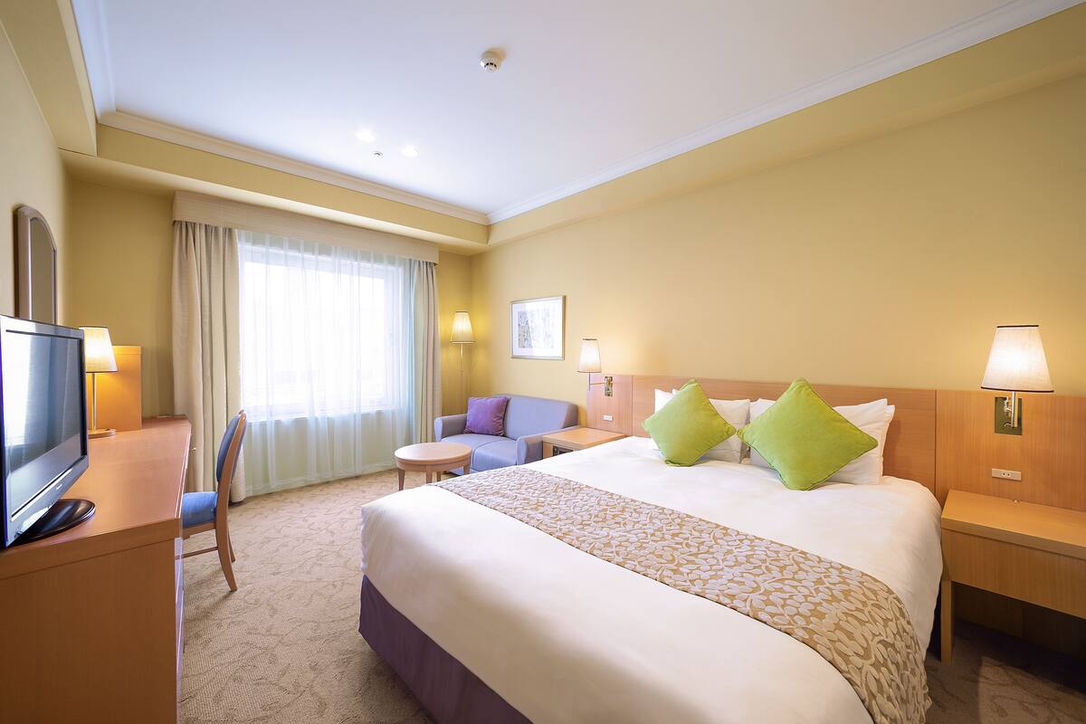 Habitación de hotel con una cama grande, un escritorio con televisor, una mesita pequeña y una silla.