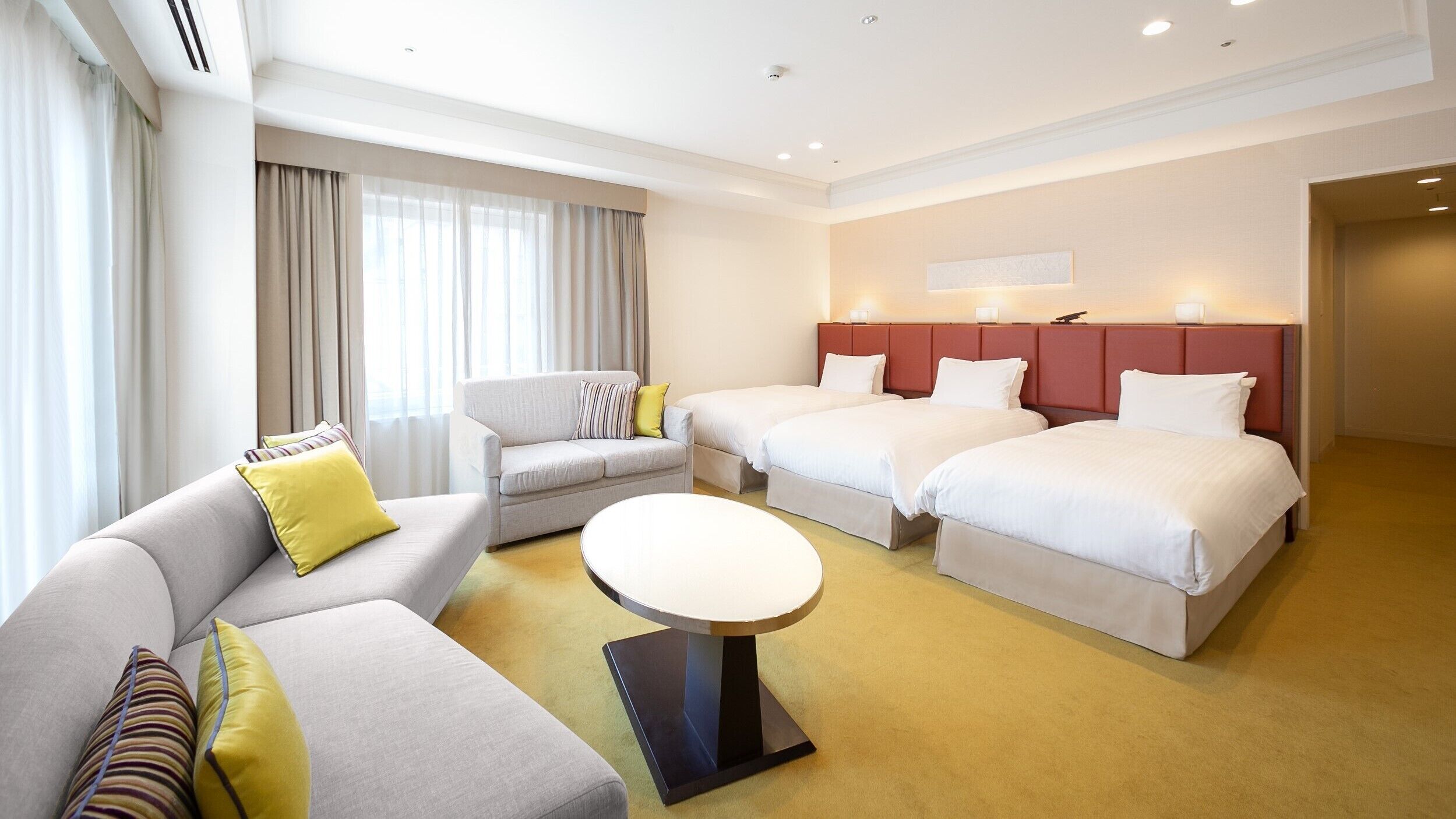 Habitación de hotel con dos camas, un sofá, una mesa redonda y una ventana con cortinas.