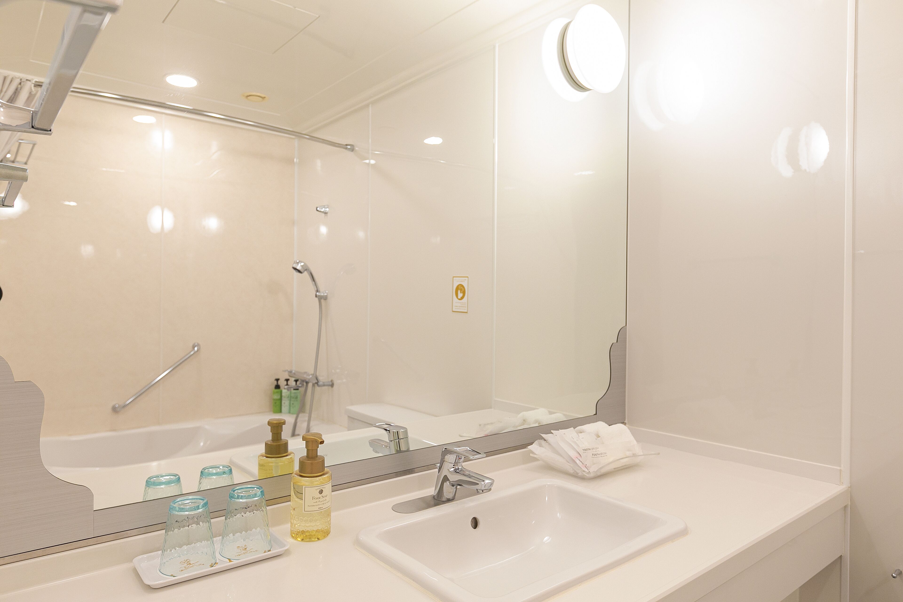A modern bathroom with a large mirror, a white sink, and a shower area.