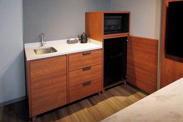 A compact kitchen with a sink, wooden cabinets, a microwave, and a dishwasher.