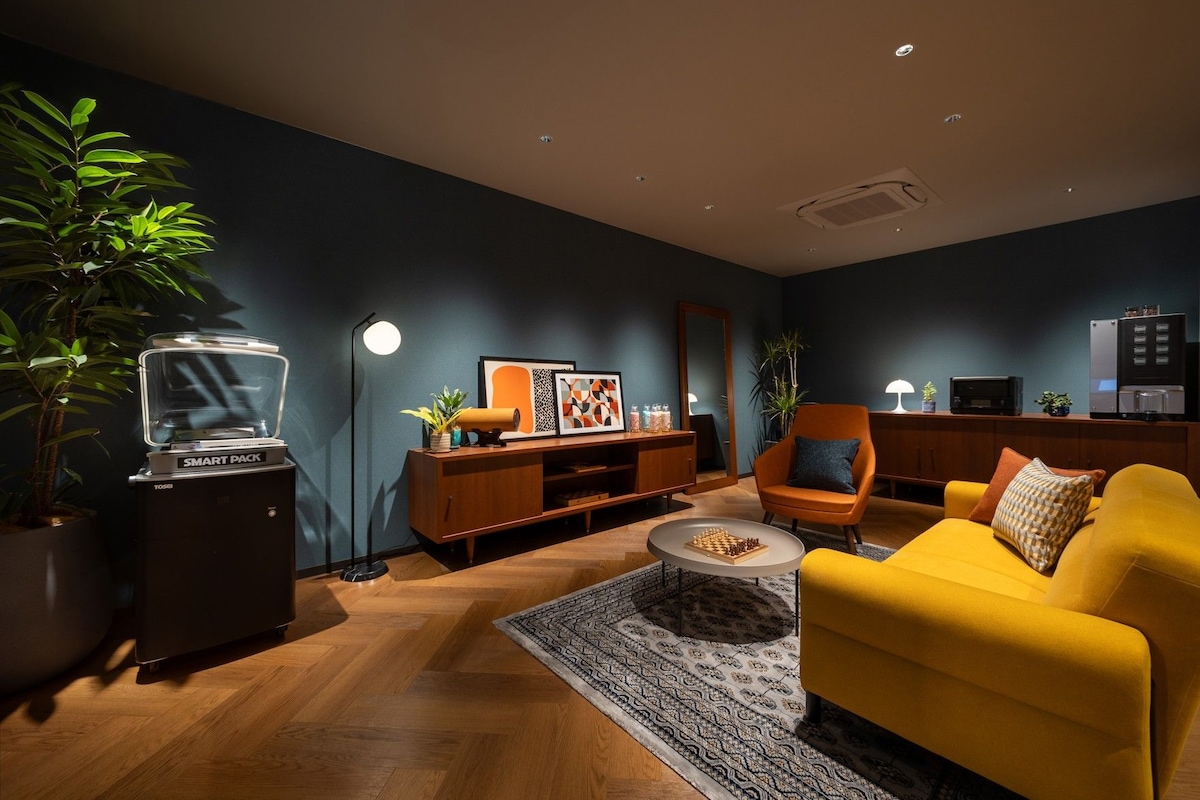 Una sala de estar moderna con un sofá amarillo, una mesa de centro de madera, una estantería y una planta grande en maceta.