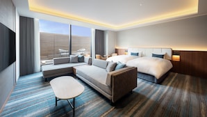 Una habitación de hotel moderna con una cama grande, un sofá, una mesita y vistas a la ciudad.