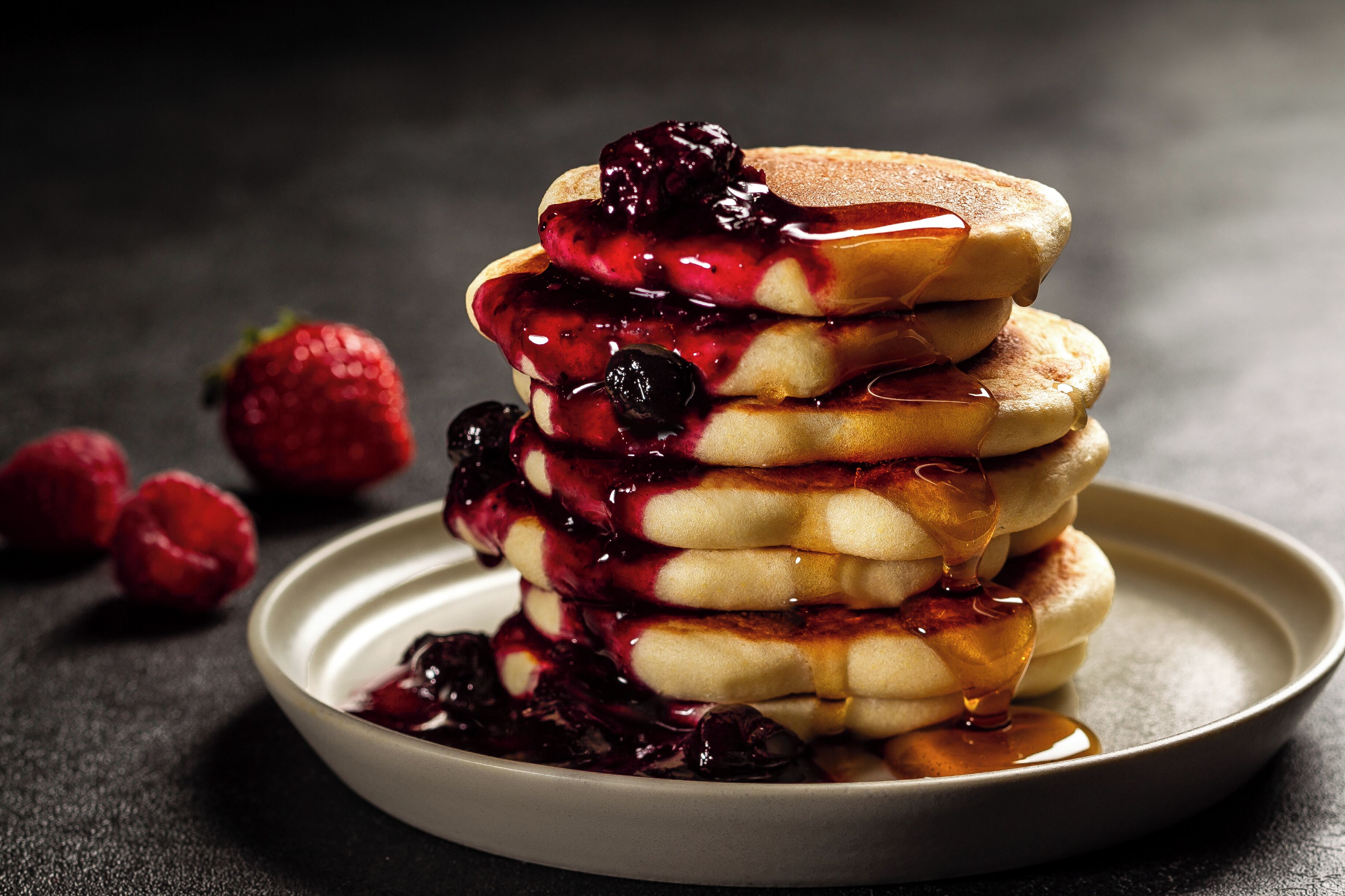 A stack of pancakes with berry compote and syrup on a plate.