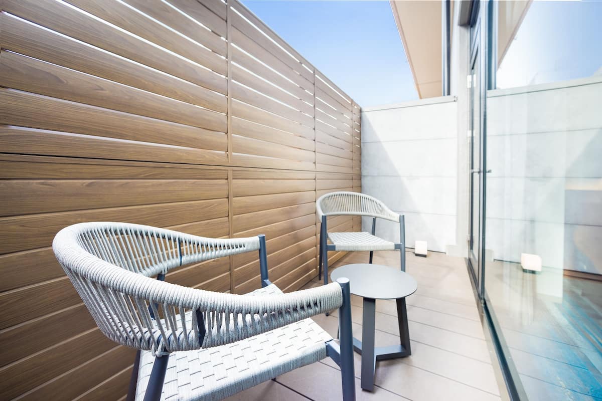 Un espace extérieur moderne, aménagé avec des chaises en osier et une petite table, un mur à lattes en bois et une cloison en verre.