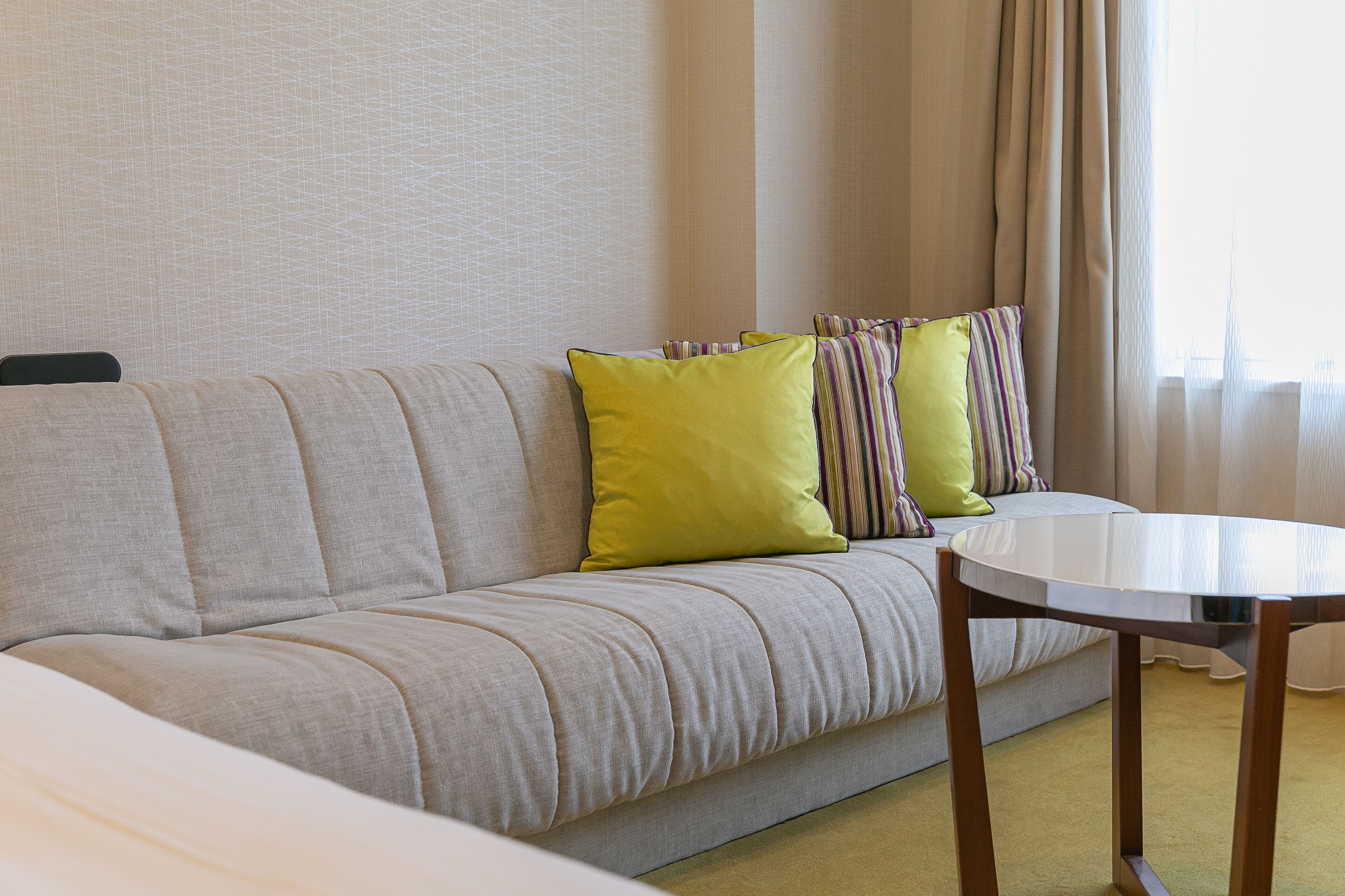 Une chambre d’hôtel avec un canapé, une table ronde et une fenêtre avec des rideaux.