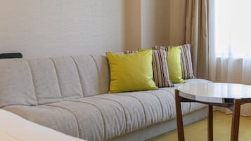 Une chambre d’hôtel avec un canapé, une table ronde et une fenêtre avec des rideaux.