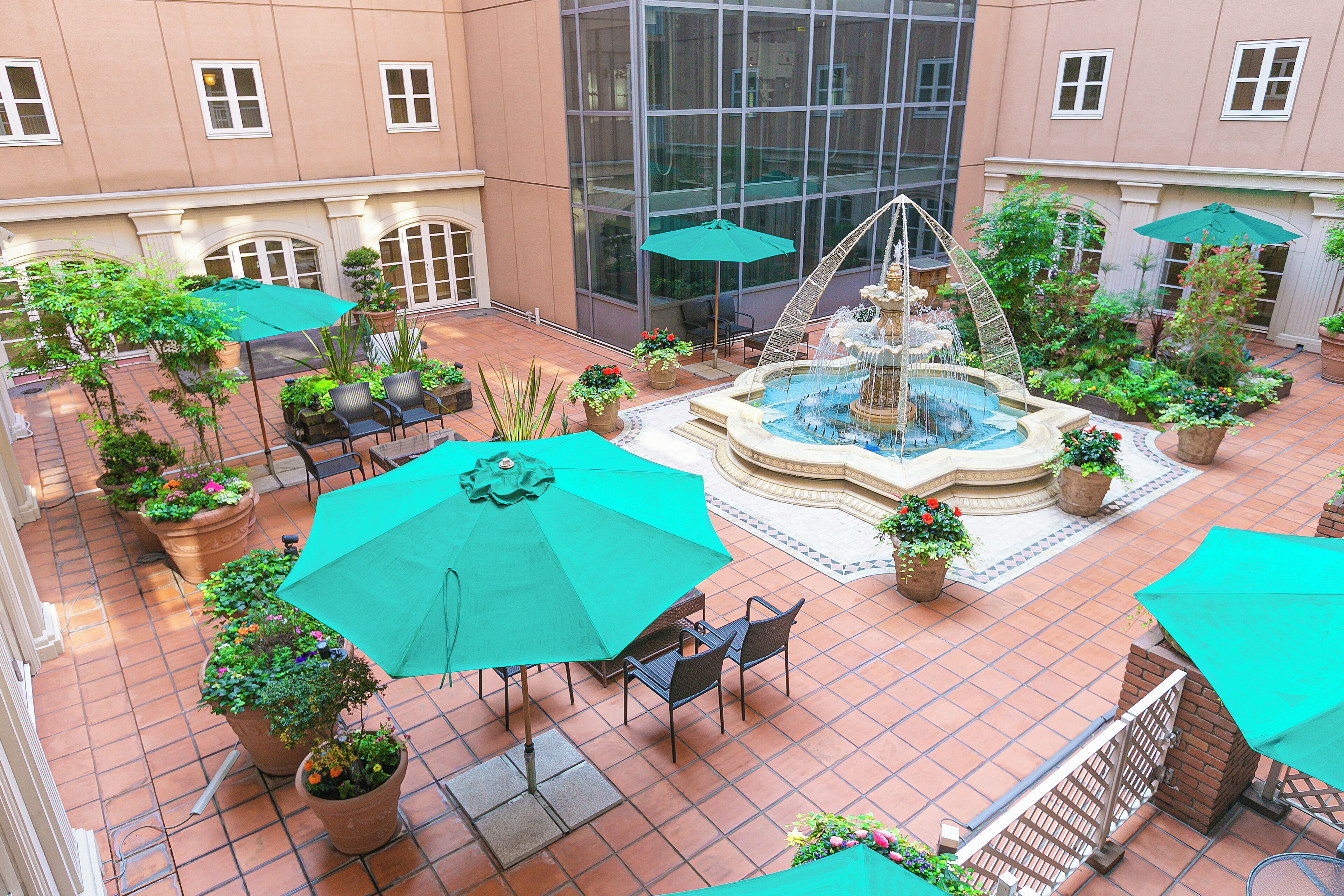 A courtyard with a central fountain, surrounded by potted plants and outdoor seating with umbrellas.