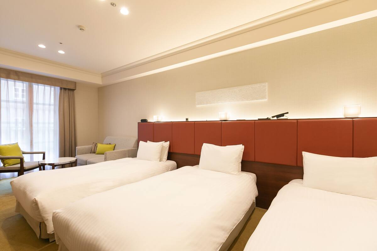 Habitación de hotel con dos camas, un escritorio, una silla y un ventanal con cortinas.