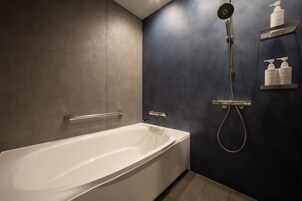 A modern bathroom with a white bathtub, a handheld showerhead, and a wall-mounted shelf with toiletries.