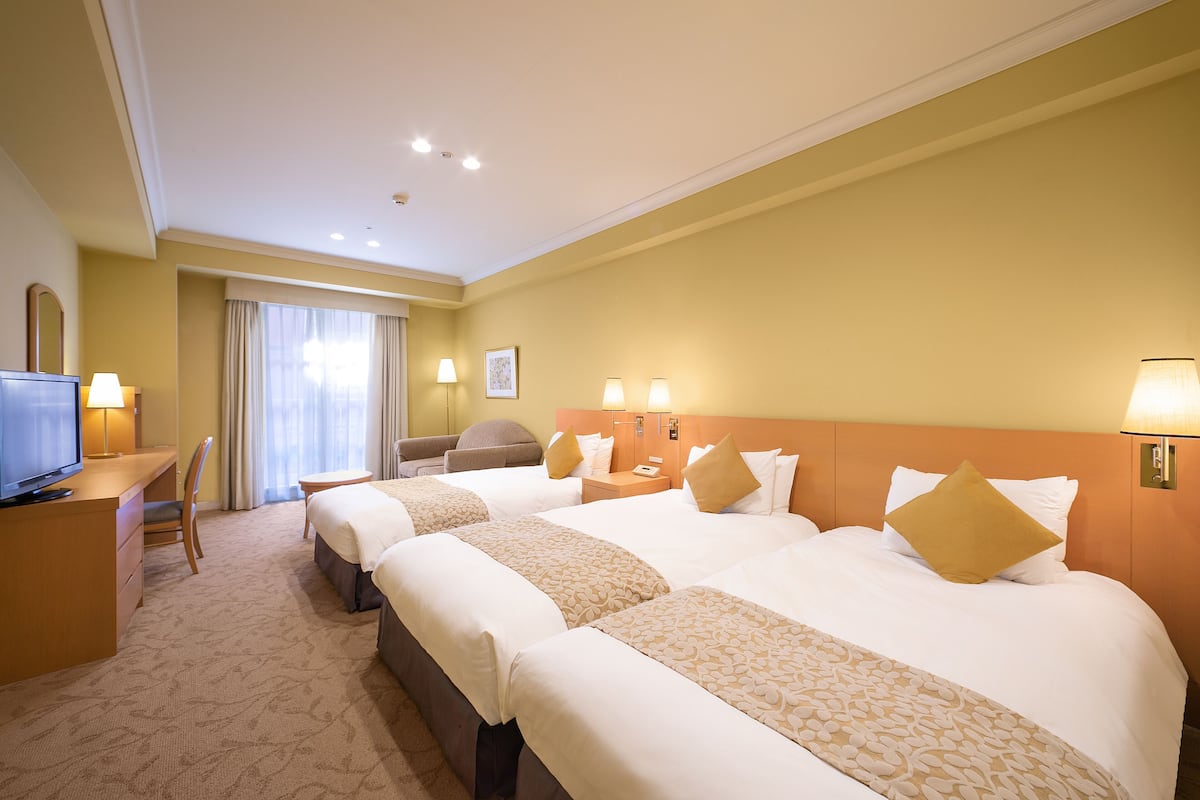 Una habitación de hotel con tres camas, un escritorio, una silla y un televisor.