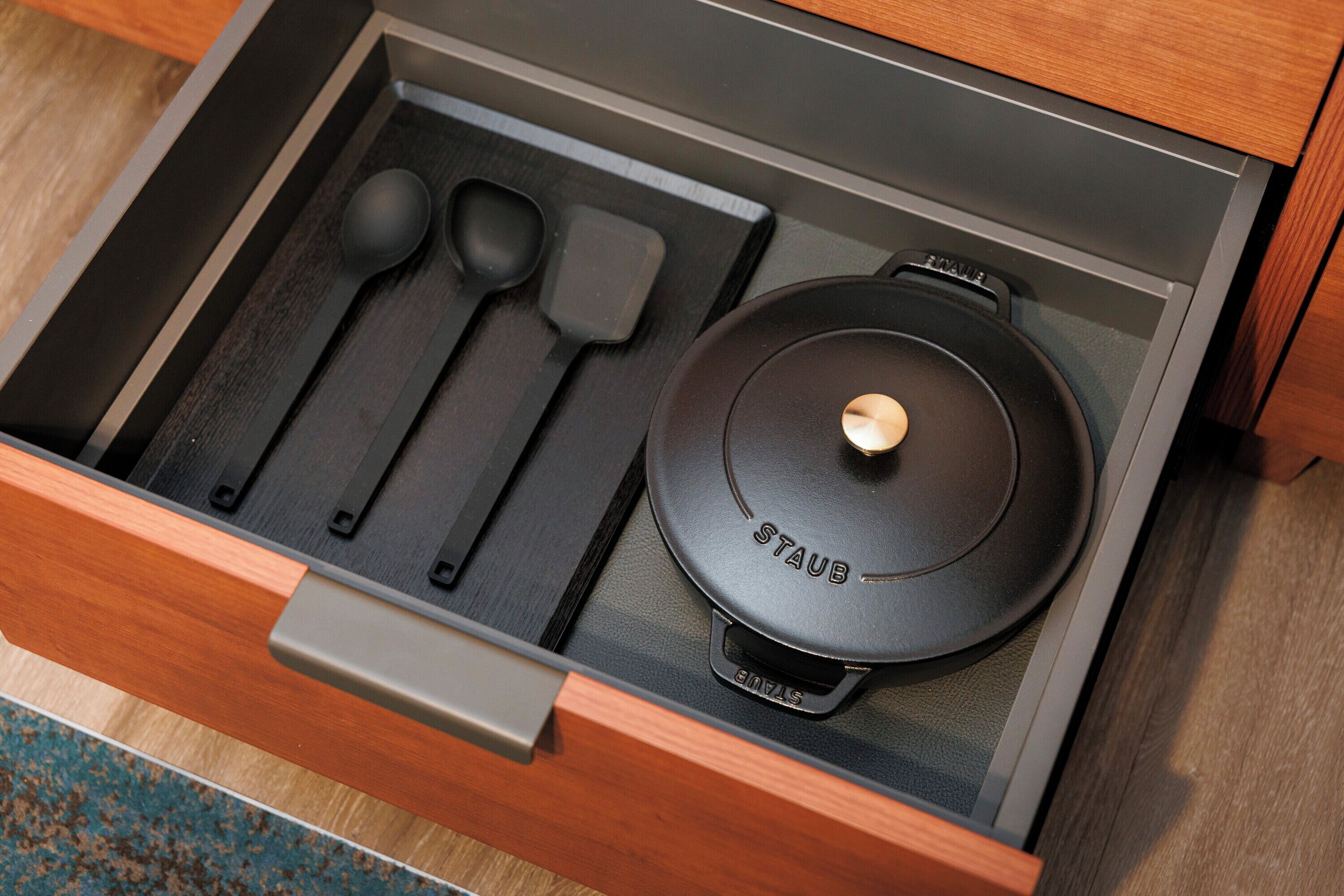 A drawer with a black pot, two black spoons, and a black spatula.