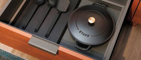 A drawer with a black pot, two black spoons, and a black spatula.