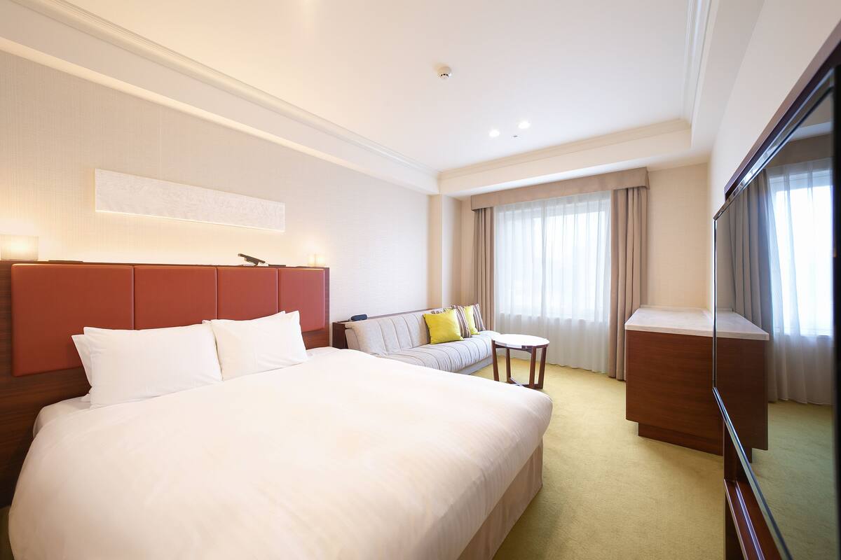 Una habitación de hotel con una cama grande, un sofá, una mesita y un televisor.