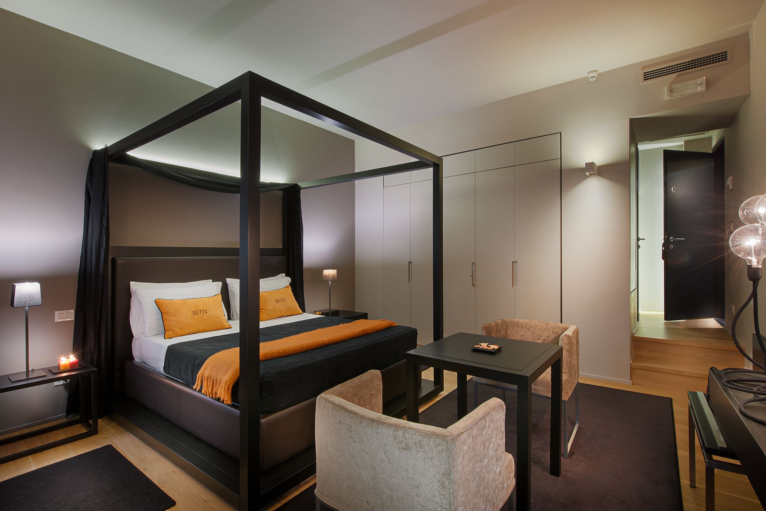 Un lit à baldaquin avec un cadre noir, une table de chevet avec une lampe, une chaise et une petite table avec une lampe.