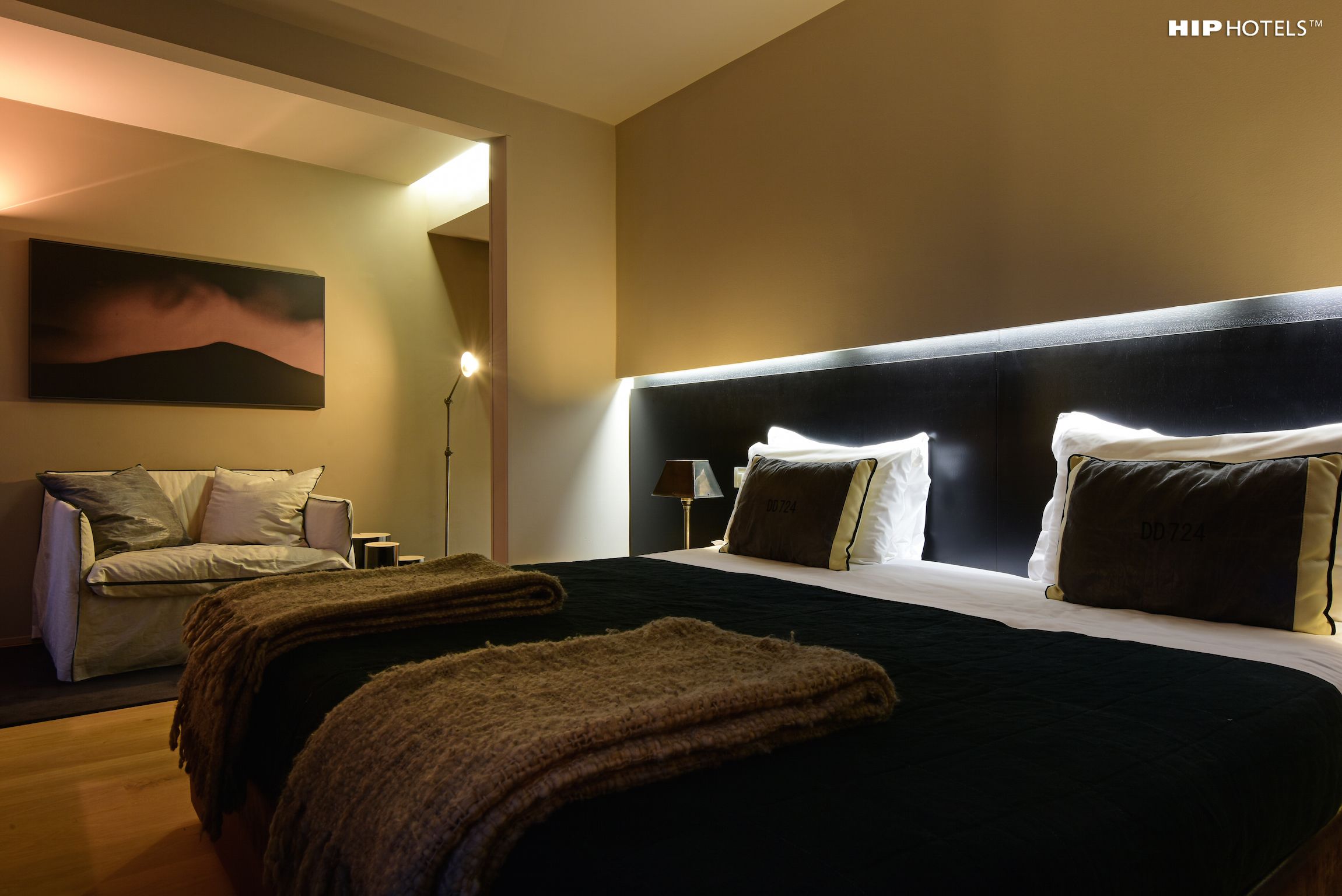 Una camera d'albergo con un letto grande, un divano, un quadro appeso e un comodino con una lampada.