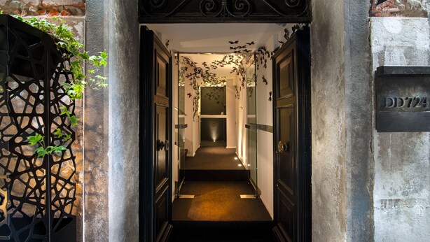Un pasillo estrecho con alfombra oscura, una reja metálica decorativa a la izquierda y una puerta con una placa de número a la derecha.