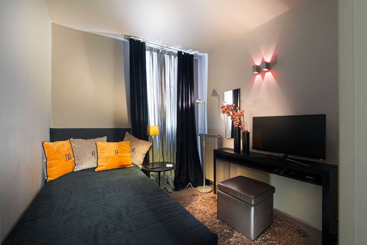 Ein Hotelzimmer mit einem Bett, einem Schreibtisch mit Fernseher, einer Lampe und einem kleinen Tisch.