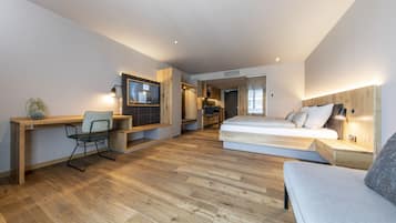 Habitació moderna i compacta amb terra de fusta, escriptori amb cadira, llit amb capçalera i petita zona de cuina.