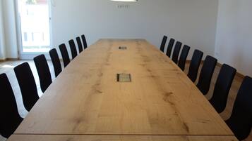 A conference room with a long wooden table, black chairs, and a black pendant light.