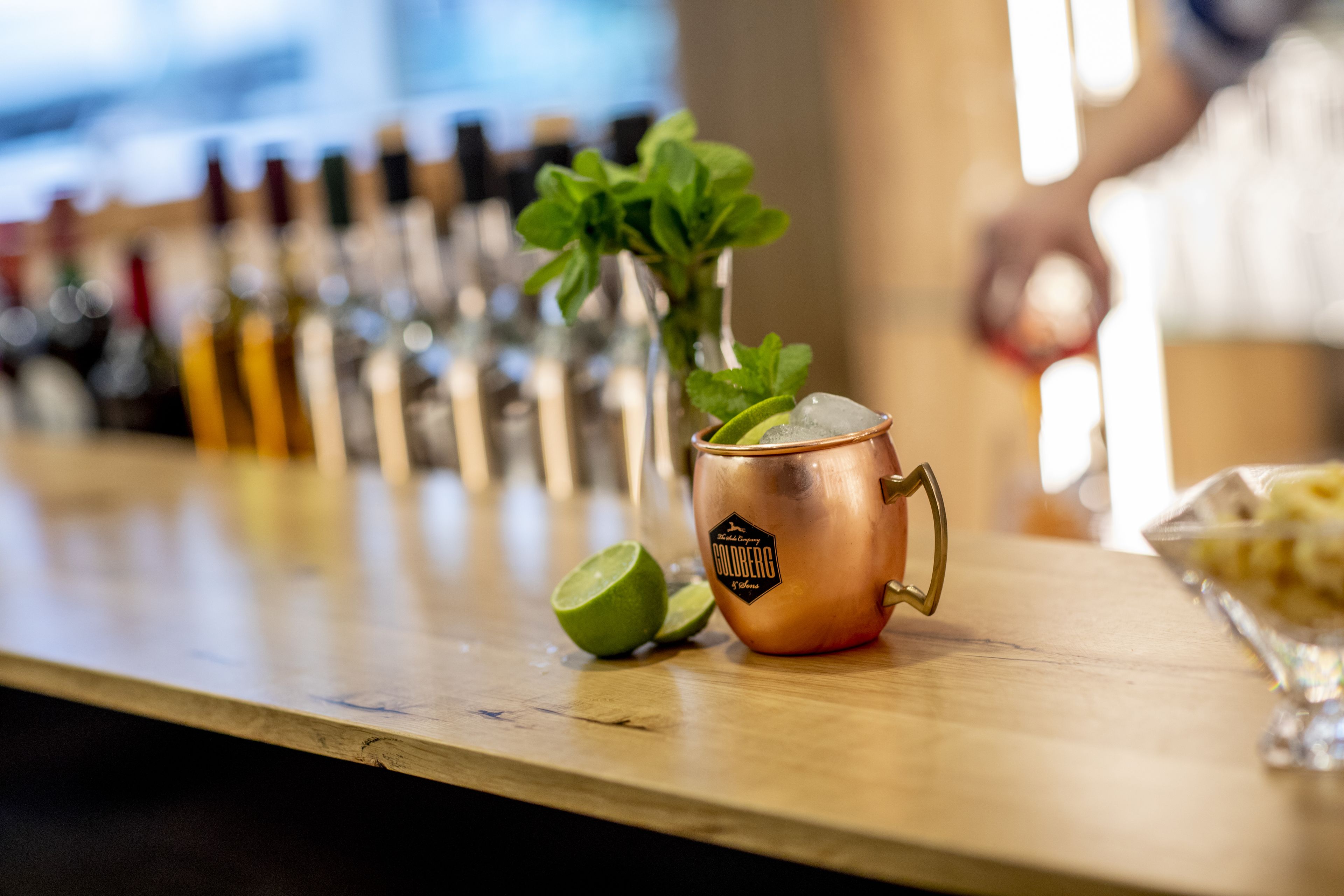 A copper mug with a mint plant on a bar counter, surrounded by bottles.