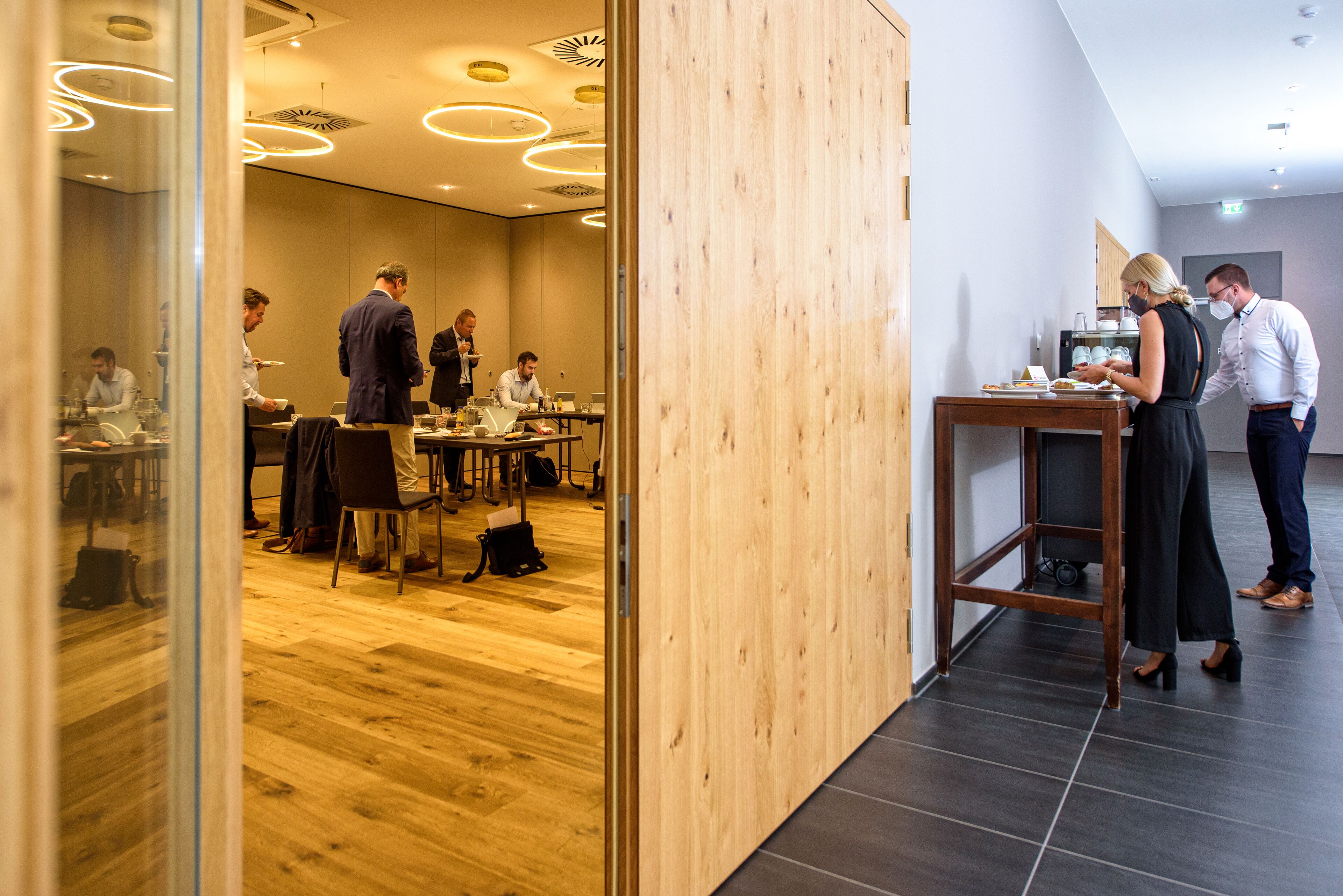 A modern conference room with wooden flooring, a glass partition, and a dining area with tables and chairs.