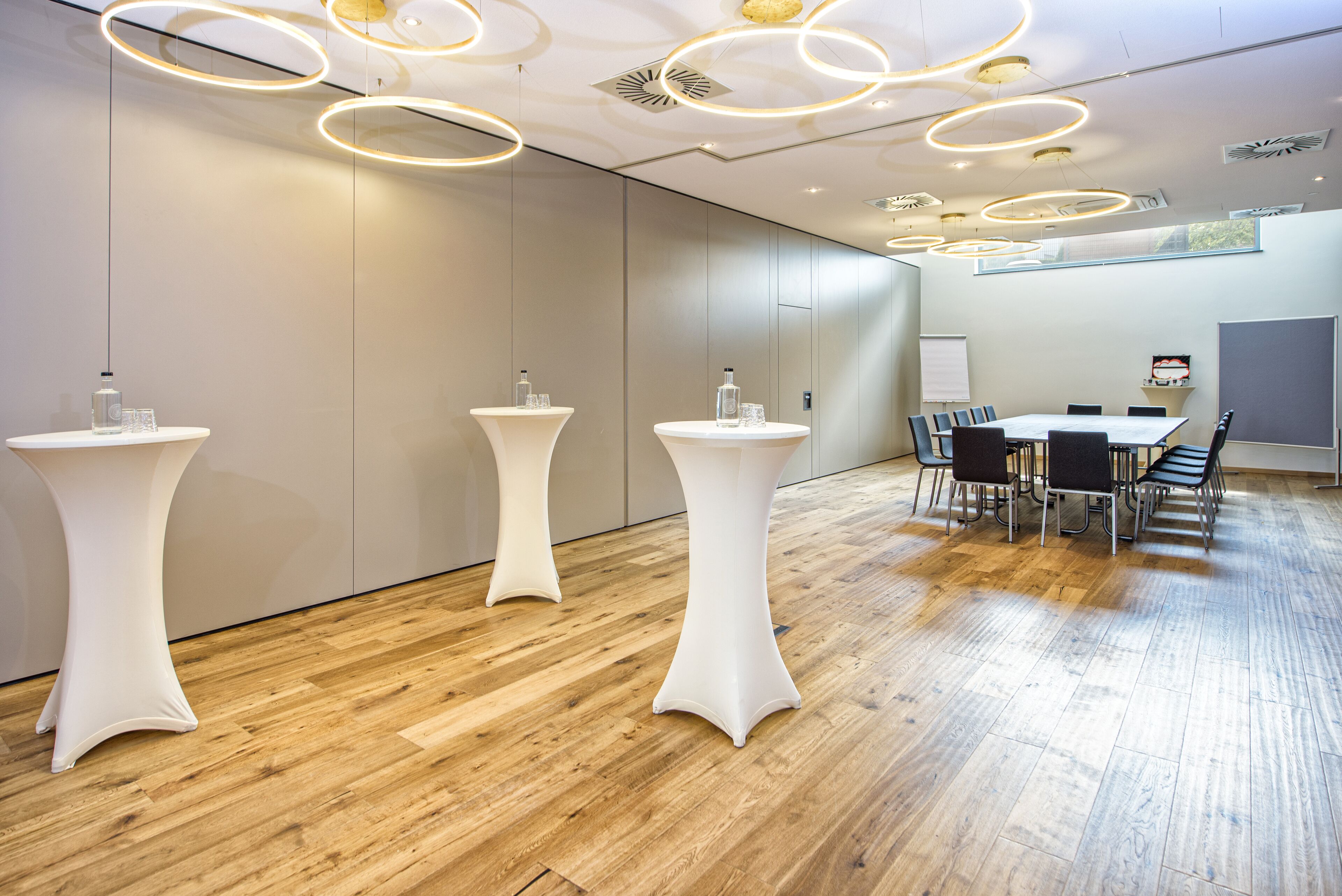A modern conference room with three white tables, a round table with chairs, and a whiteboard on the wall.