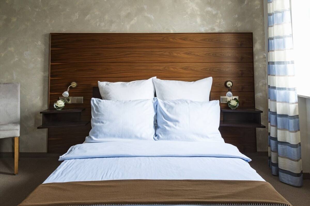 Un lit bien fait, avec du linge de lit blanc, une tête de lit en bois et deux tables de chevet ornées de lampes et d’objets décoratifs.