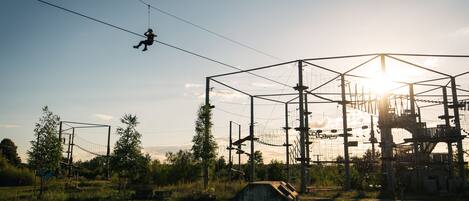 A person zip-lining across a clear sky with a sunlit structure in the background.