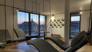 Een moderne woonkamer met een groot raam, een bank, een fauteuil en een wand versierd met ronde spiegels.