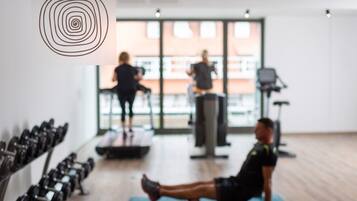 Uma academia com esteiras, halteres e uma pessoa executando um exercício de prancha.