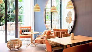 Een modern interieur met rieten hanglampen, een ronde spiegel en een zithoek met oranje kussens en een ronde tafel.