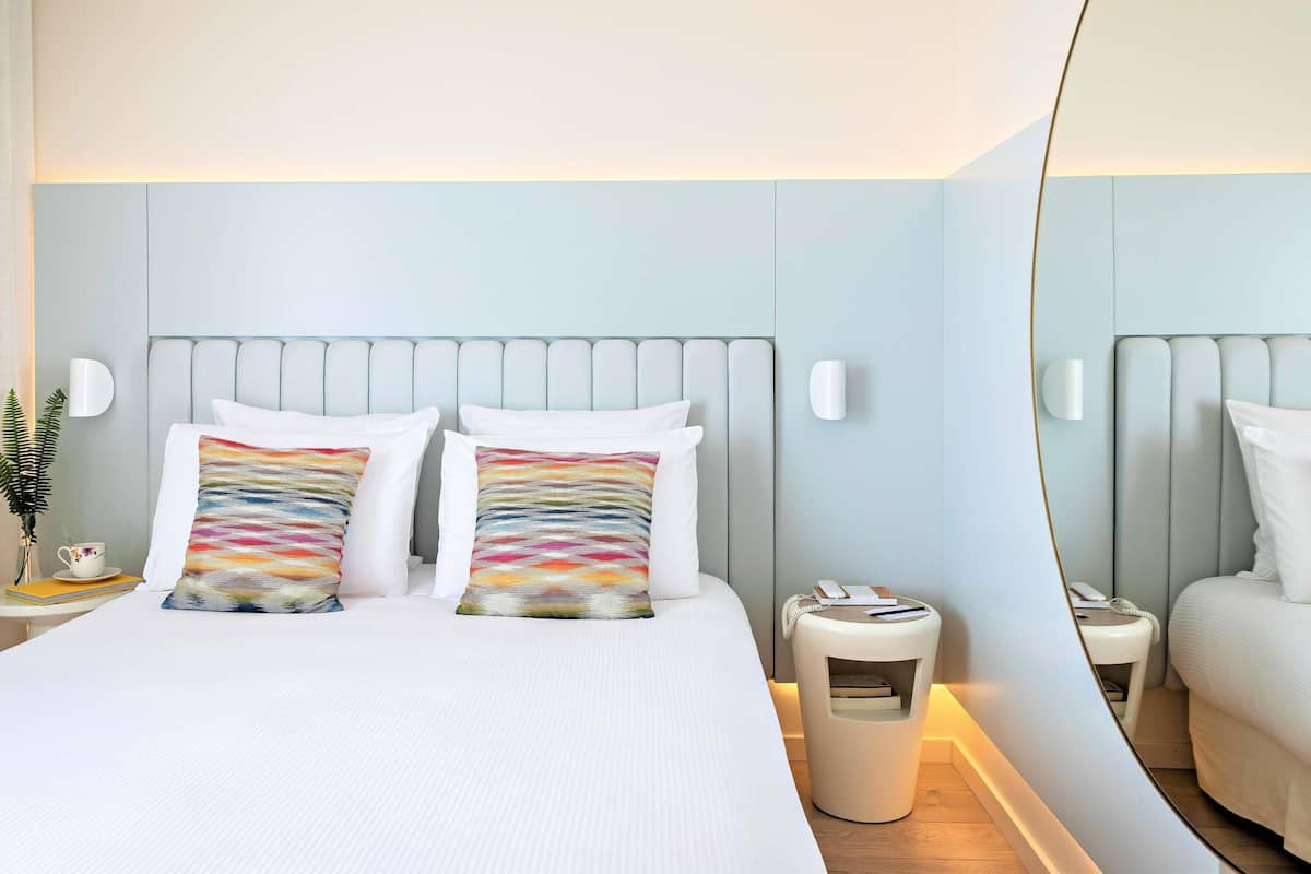 Ein Hotelzimmer mit Bett, Nachttischen, einem Spiegel und einem Mülleimer.