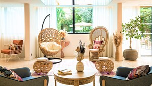 Een moderne woonkamer met rieten meubels, een ronde houten tafel en grote ramen met uitzicht op de omgeving.