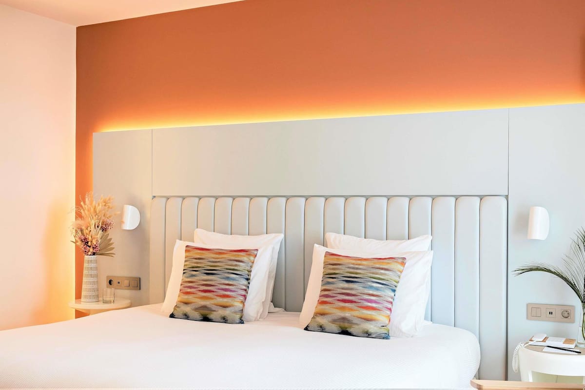 Ein Hotelzimmer mit einem Bett, zwei Kissen, einem Nachttisch mit einer Vase und einem an der Wand befestigten Telefon.