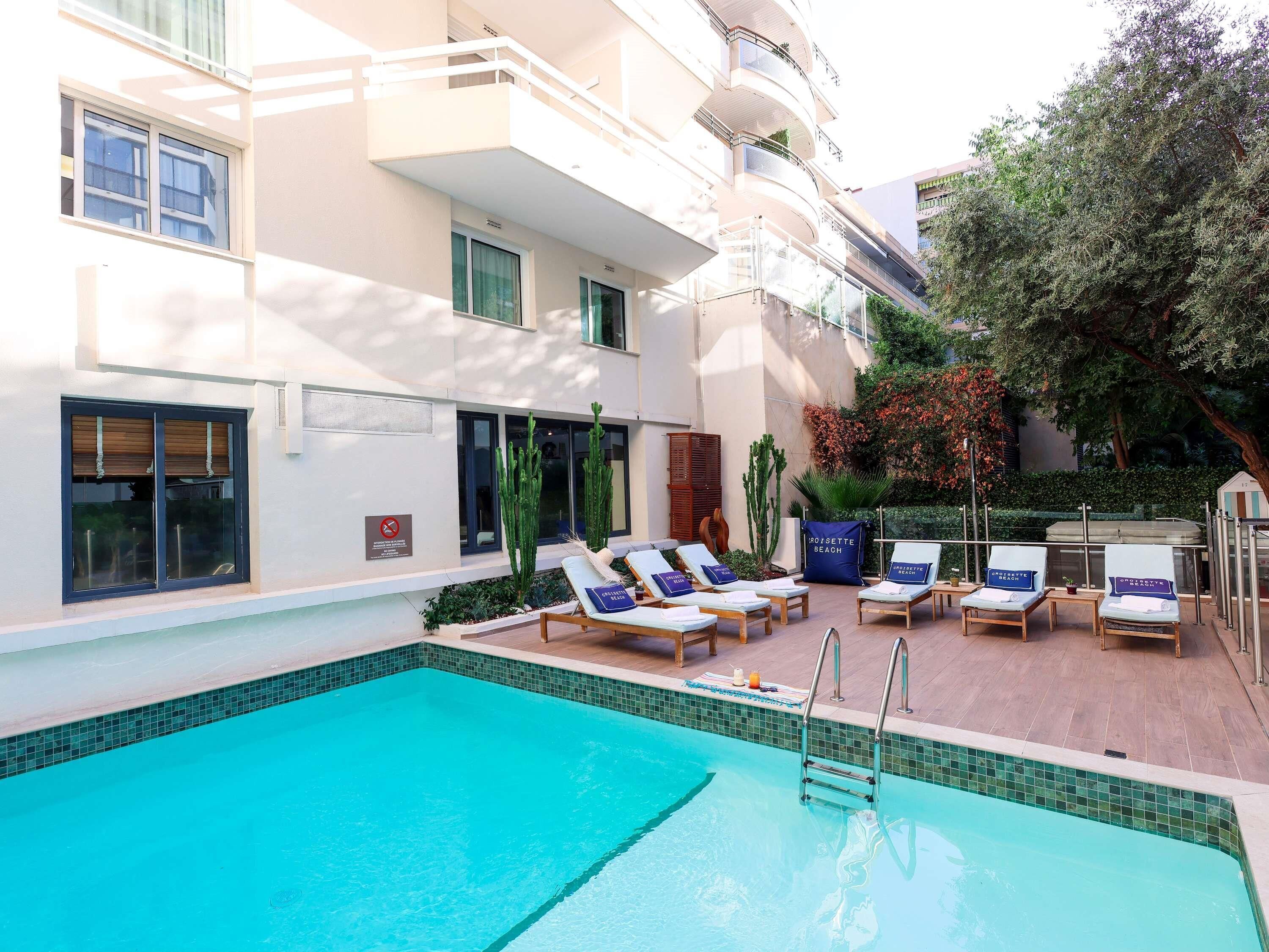 A pool area with lounge chairs, a pool ladder, and a building with balconies.