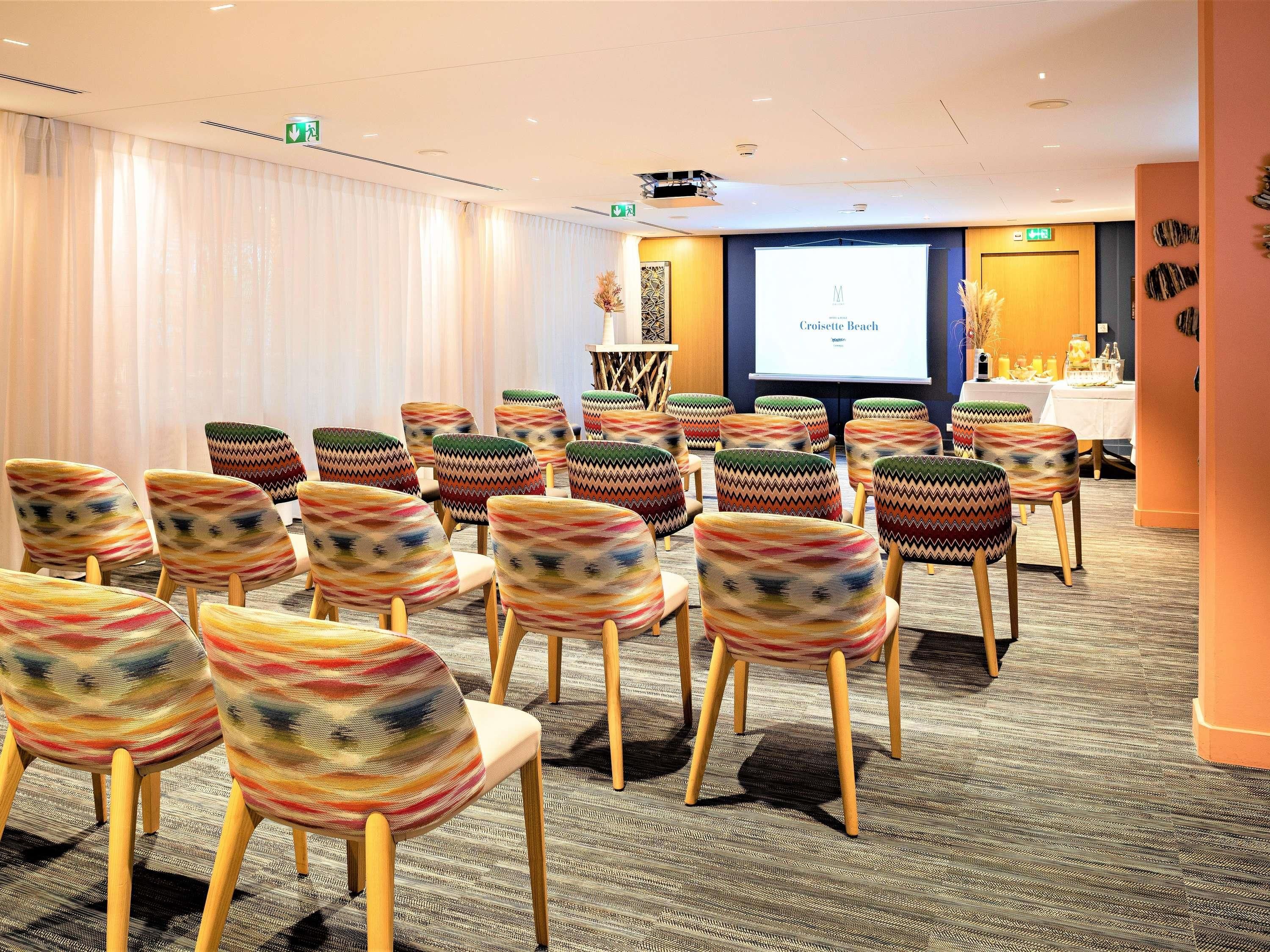 A conference room with rows of chairs, a projector screen, and a table with a floral arrangement.