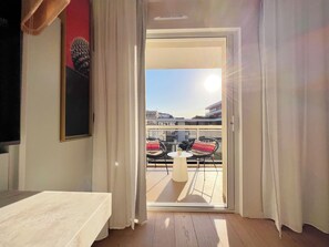 A hotel room with a bed, a small table, and a view of the city through a glass door.