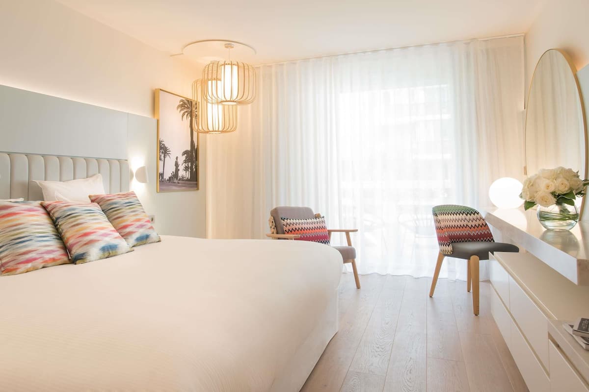 Ein modernes Hotelzimmer mit einem großen Bett, einem Schreibtisch, einem Stuhl, einem Spiegel und einem Fenster mit durchsichtigen Vorhängen.