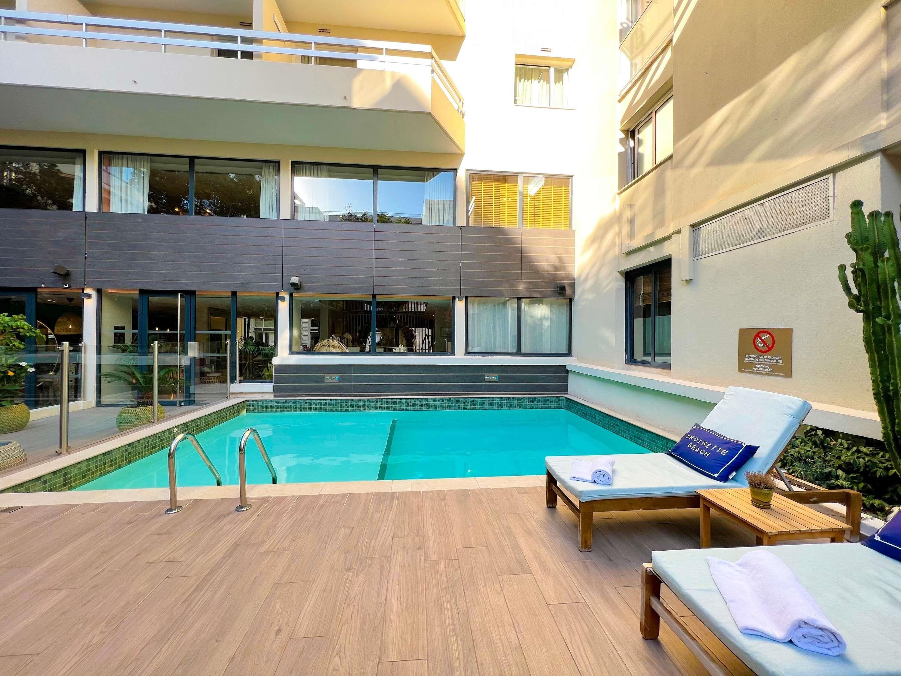 Una piscina al aire libre, sombrillas, sillones reclinables de piscina