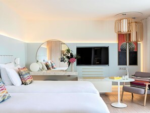 A modern hotel room with a large bed, a TV, a small table, and a seating area.