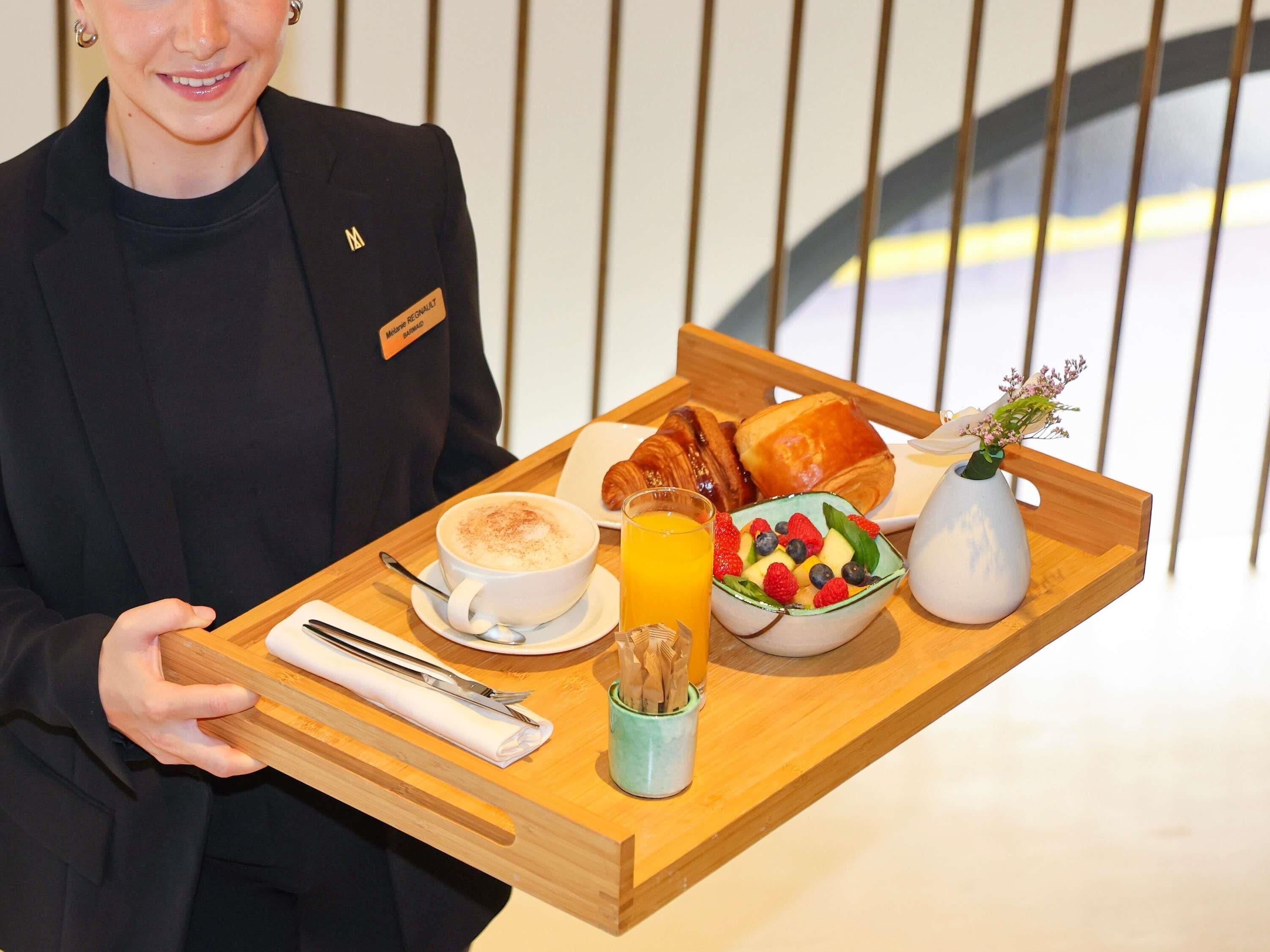 A tray with breakfast items including croissants, a bowl of fruit, a glass of orange juice, and a cup of coffee.